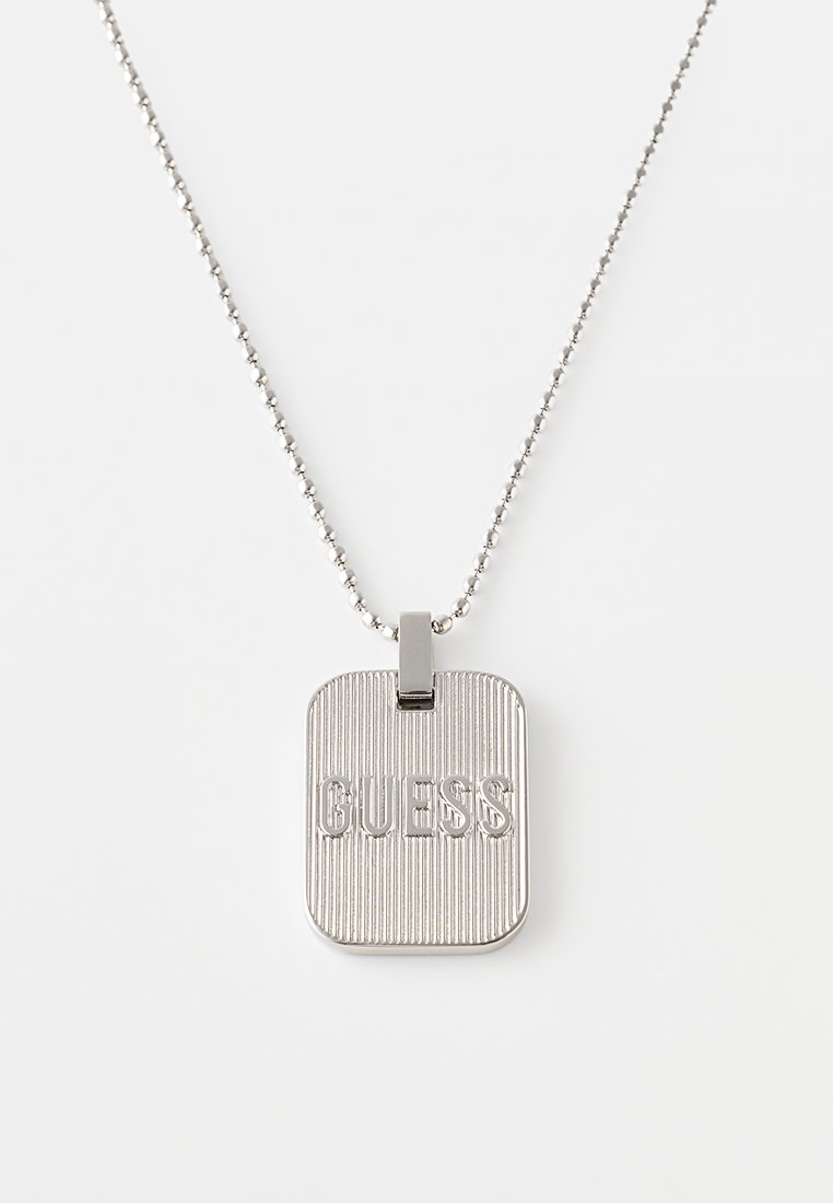 Zilveren hanger ketting met een rechthoekig label met ribbelstructuur en het woord "GUESS" in reliëf, bevestigd aan een kralenketting.