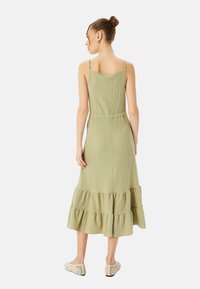 Abito verde chiaro, lungo fino al ginocchio, con spalline regolabili, tessuto texture e orlo a balze. Indossato con scarpe chiare e con motivo.