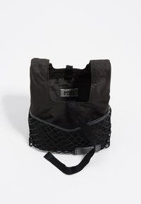 Bolsa de tote negra de nailon con una sección inferior de malla. Presenta un asa superior, etiqueta interna y textura suave. Elemento de diseño minimalista.
