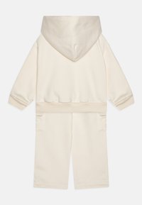 Set din hanorac și pantaloni scurți de culoare crem, realizat dintr-un material moale, având un glugă mare, buzunare laterale și manșete și talie cu dantelă.