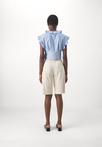 Blouse à rayures bleu clair, à volants, avec une taille cintrée, assortie à un short beige longueur genou. Sandales à talons noires en vedette.