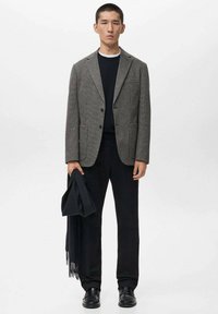 Grau meliertes Blazer mit Reverskragen, zwei vorderen Taschen, kombiniert mit einem schwarzen Pullover, schwarzen Hosen und einem schwarzen Schal, alles ordentlich gestylt.