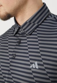 Short-sleeve gray polo shirt with horizontal and vertical stripes, button closure, pointed collar, and distinctive logo on the left chest.