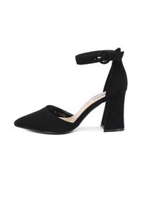 Tacchi alti in suede nero con punta affusolata e cinturino alla caviglia dotato di una fibbia circolare. Il tacco è spesso e strutturato, migliorando la stabilità.