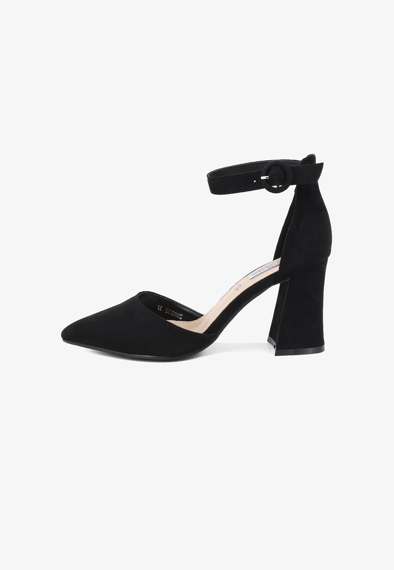 Tacchi alti in suede nero con punta affusolata e cinturino alla caviglia dotato di una fibbia circolare. Il tacco è spesso e strutturato, migliorando la stabilità.