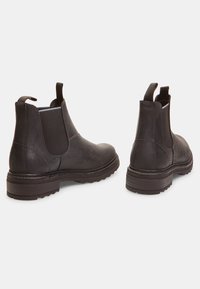 Botas Chelsea de cuero negro con paneles elásticos a los lados, punteras redondeadas y suelas de goma texturizadas para mayor tracción. Presentan una pestaña de tira en la parte trasera.