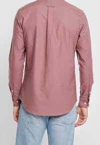 Långärmad skjorta, mjuk rosa tyg, skräddarsydd design med knappmanschetter, ryggen med veck, rundad nederkant, tillsammans med ljusblå jeans.