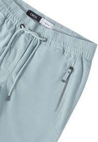 Pantalon bleu clair avec une taille élastique, fermeture à cordon, et une poche latérale zippée. Tissu texturé. Marque : CECIL.