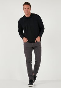Polo negro de manga larga con tapeta de botones, combinado con pantalones ajustados gris y zapatillas negras con cierre de velcro.