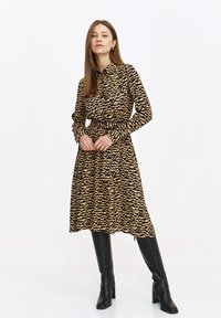 Langärmliges Hemdkleid im schwarz-beige Wellenmuster, mit Kragen, einem Gürtel in der Taille und fließendem Stoff bis zur Kniehöhe.