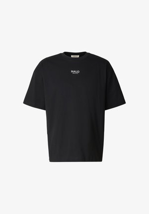 Mężczyzna stojący tyłem, ubrany w czarną koszulkę z białym napisem "OFF DUTY GEAR" i dużą zieloną grafiką karabinka na plecach.