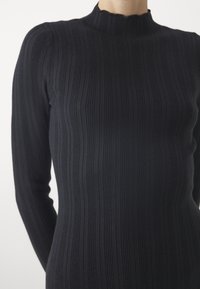 Top negro de canalé con mangas largas y cuello de tortuga con puntas en forma de ola. La textura es suave y ajustada al cuerpo.