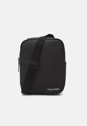 Petit sac bandoulière noir Calvin Klein avec sangle réglable et fermeture éclair, présenté sur un fond blanc.