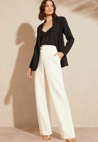Zwarte blazer met een getailleerd ontwerp, bovenstuk met kantafwerking, hooglopende witte wijde broek en beige haksandalen. Soepele textuur, strakke lijnen.