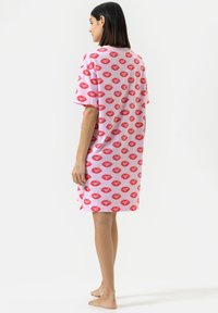 Abito t-shirt oversize rosa con un motivo di labbra rosse ripetuto. Maniche corte, tessuto morbido, lunghezza al ginocchio e vestibilità ampia.