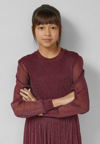 Bordowa sukienka z połyskującą fakturą, długimi przezroczystymi rękawami i okrągłym dekoltem. Spódnica jest plisowana, co tworzy lekki, zwiewny wygląd.