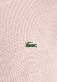 Sweater em lã rosa com um pequeno logótipo de crocodilo verde bordado na área do peito esquerdo. Tecido texturizado com um acabamento suave.