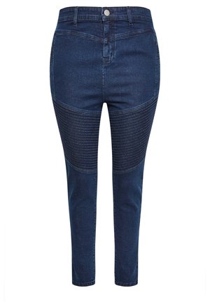 Tummansiniset farkut, joissa on korkea vyötärö, ja jotka ovat varustettu teksturoiduilla ribbipaneeleilla reiden alueella sekä hoikalla istuvuudella nilkoissa.