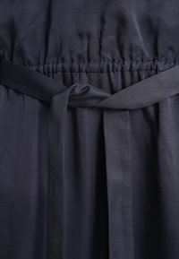 Tissu de robe bleu marine avec une ceinture froncée, avec une ceinture assortie nouée à l'avant, texture lisse, détails de couture minimalistes.