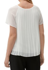 Blouse blanche plissée à manches courtes, avec un col rond et un tissu léger et fluide. La vue arrière montre un drapé doux et une coupe décontractée.