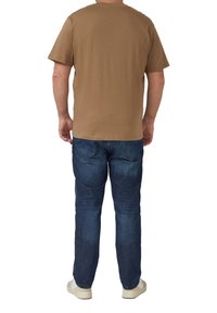 Brązowy bawełniany t-shirt z okrągłym dekoltem i krótkimi rękawami, w połączeniu z ciemnoniebieskimi dżinsami i białymi trampkami, widziany od tyłu.