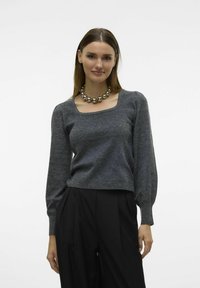 Grau strukturiertes Sweatshirt mit quadratischem Ausschnitt und langen Ärmeln, kombiniert mit schwarzen Hosen und einer Kette aus metallischen Perlen.