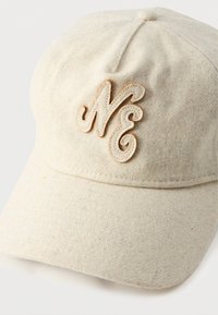 Cream-colored cap made of felt material featuring a curved brim and a stitched "NE" logo in tan on the front. Textured and soft finish.