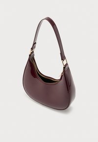 Sac à main en cuir verni bordeaux avec une forme courbée, une anse unique et un détail de fermeture éclair dorée sur l'ouverture supérieure, présentant une texture lisse.