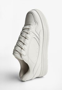 Adidaș alb din piele netedă cu accente din plasă texturată, având un vârf rotund, șase găuri pentru șireturi și o talpă groasă, striată.