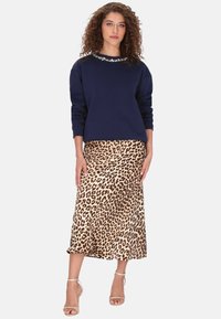 Bluză de trening bleumarin cu guler împodobit cu pietre, asortată cu o fustă midi cu imprimeu de leopard. Textură netedă, croială lejeră și sandale cu baretă la gleznă.