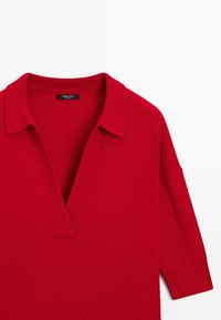 Czerwona dzianinowa sweterka z głębokim dekoltem w kształcie V i kołnierzykiem, z długimi, prążkowanymi rękawami, leżąca na białym tle.