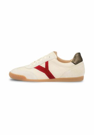 Lage witte sneaker met een rode zijstreep, lichtbruine zool, witte veters en een getextureerd donkerbruine hielstuk.