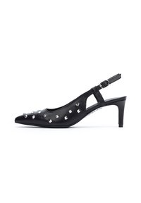 Zapato de tacón negro tipo slingback, hecho de piel suave con punta afilada. Presenta tachuelas plateadas a lo largo del lateral y un tacón delgado. Incluye una correa ajustable.