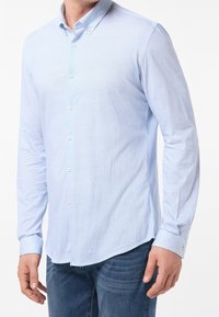 Jasnoniebieska koszula z długim rękawem zapinana na guziki, z текстurowanym wzorem, standardowym kołnierzykiem i białymi guzikami. Zaokrąglony dół i mankiety zapinane na jeden guzik.