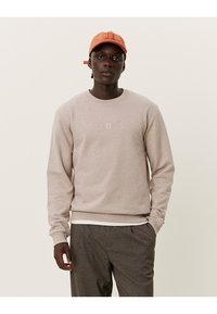 Beige sweatshirt met een ronde hals en een minimalistisch "II" logo op de borst. Zachte textuur, gecombineerd met een geruite broek en een oranje pet.