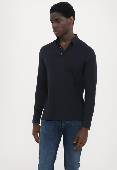 Ναυτικό μακρυμάνικο πόλο μπλουζάκι με γιακά, κουμπί και ριγέ μανσέτες, συνδυασμένο με μπλε τζιν. Λείο υλικό, κλασική εφαρμογή.