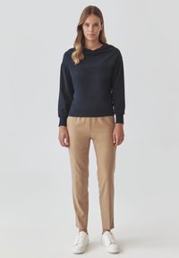 Marineblauer Kapuzenpullover mit langen Ärmeln, kombiniert mit sandfarbenen, taillierten Hosen und weißen Sneakers. Glatte Stofftextur, minimalistisches Design.
