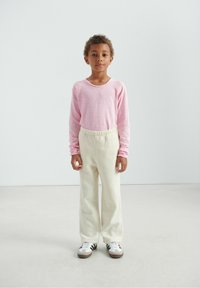 Pull rose à manches longues avec un col rond, associé à un pantalon en polaire couleur crème et des baskets blanches à rayures noires.