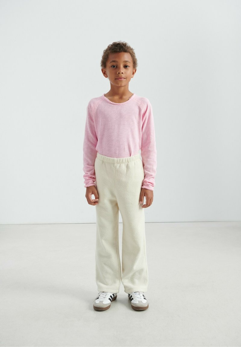 Pull rose à manches longues avec un col rond, associé à un pantalon en polaire couleur crème et des baskets blanches à rayures noires.