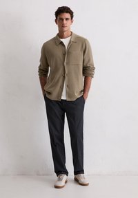 Lichtbruine button-up shirt met een borstzak, gecombineerd met donkergrijze broeken en beige sneakers. Gladde stof, ontspannen pasvorm, casual stijl.