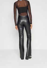 Pantalon évasé en similicuir noir avec une texture lisse et des poches, doté d'une taille ajustée et de plis subtils le long des jambes.