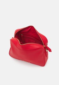 Borsa in pelle rossa con texture gommosa, forma arrotondata, cerniera dorata e interno aperto che mostra una piccola tasca e rivestimento tonale.