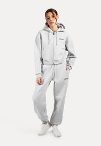 Felpa grigia in cotone con zip frontale e due tasche, abbinata a pantaloni della tuta coordinati con polsini elasticizzati e dettagli con logo.