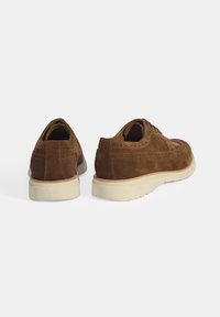 Chaussures en daim brun avec un design brogue, un bout arrondi et une semelle en caoutchouc de couleur claire avec des coutures définies.