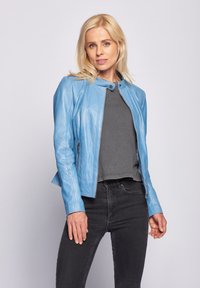 Ljusblå läderjacka med hög krage, dragkedja och sidofickor. Bärs över en grå topp och tillsammans med svarta jeans.