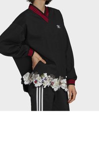 Mustat ylisuuret collegepaidat, joissa on punaiset raidalliset V-pääntvät, broderad kukkakuvioinen pitsikuvio helmassa ja valkoinen logo rinnassa.