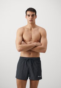 Pantaloni scurți de înot negri, cu talie elastic�ă și șnur, având un material texturat și un mic logo alb în partea stângă jos.