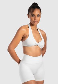 Ljusgrå sport-BH med en vriden framsida och halterneck. Kombineras med högmidjade, släta grå shorts.