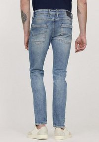 Jean en denim bleu clair avec une coupe slim, avec une taille mi-haute, cinq poches et un léger délavage. Associés à des baskets de couleur crème.