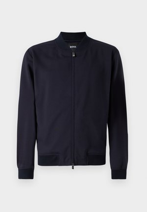 Sötétkék bomber dzseki sima anyagból, cipzáras záródással, állógallérral, bordás mandzsettával és alsó szegéllyel. Nincsenek látható minták vagy díszítések.
